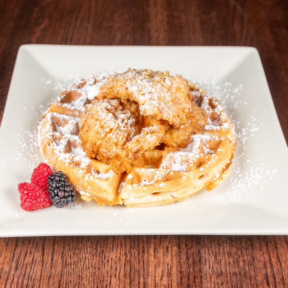 Chicken and waffles dusted with powdered sugar, garnished with raspberries and blackberries.