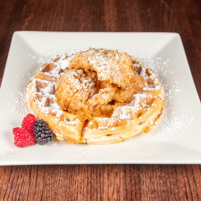 Chicken and waffles dusted with powdered sugar, garnished with raspberries and blackberries.