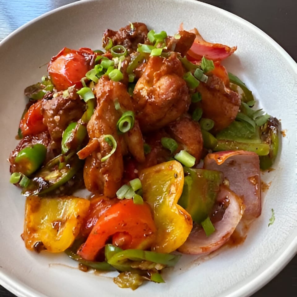Himalayan Cuisine's chili chicken with bell peppers, onions, and scallions in a white bowl.