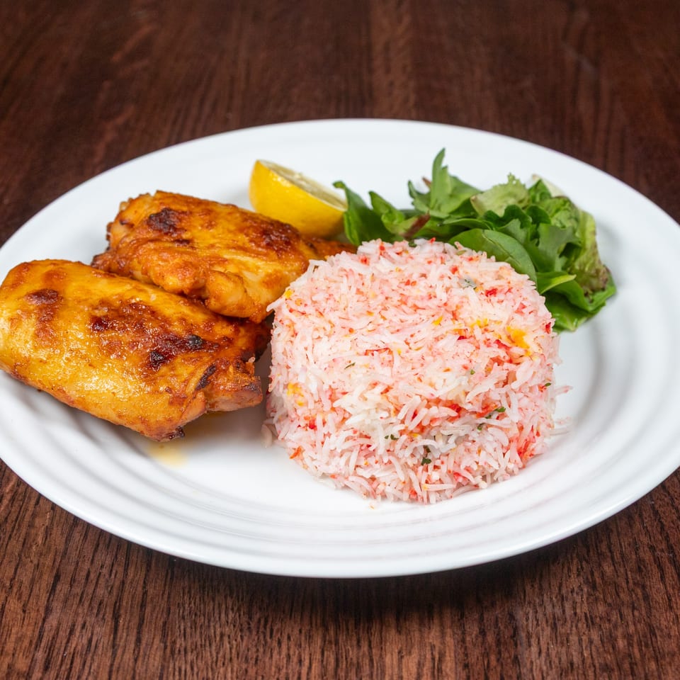Nepalese chicken dish with colorful rice, a lemon wedge, and greens on a white plate.