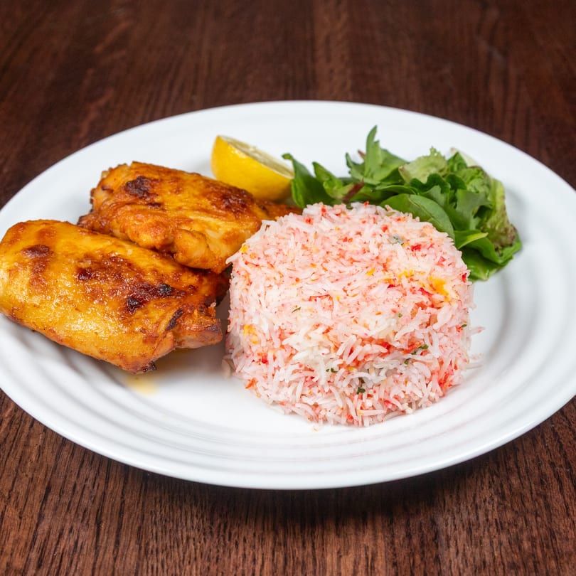 Nepalese chicken dish with colorful rice, a lemon wedge, and greens on a white plate.