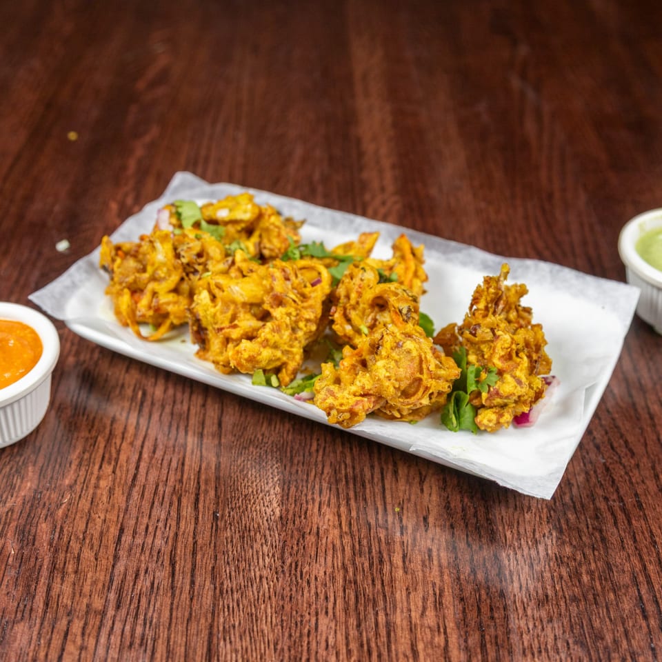 A plate of golden-brown Nepalese pakora, garnished with cilantro, served with two dipping sauces.
