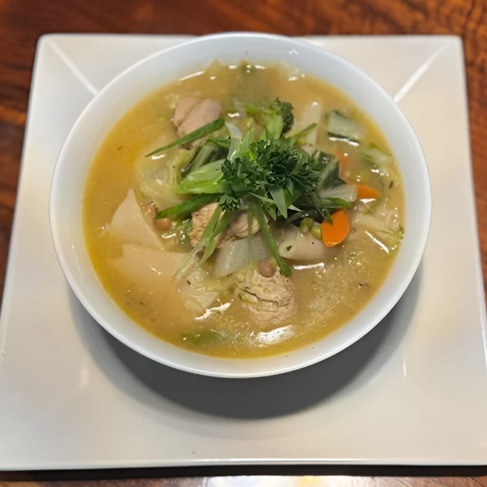 A bowl of Nepalese chicken and vegetable soup, garnished with fresh herbs, on a white plate.