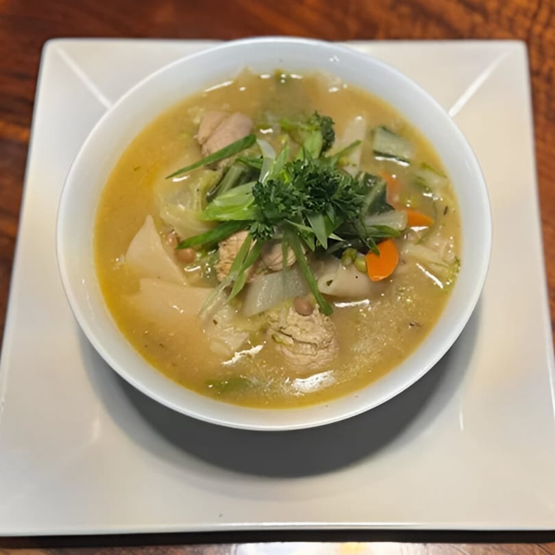 A bowl of Nepalese chicken and vegetable soup, garnished with fresh herbs, on a white plate.