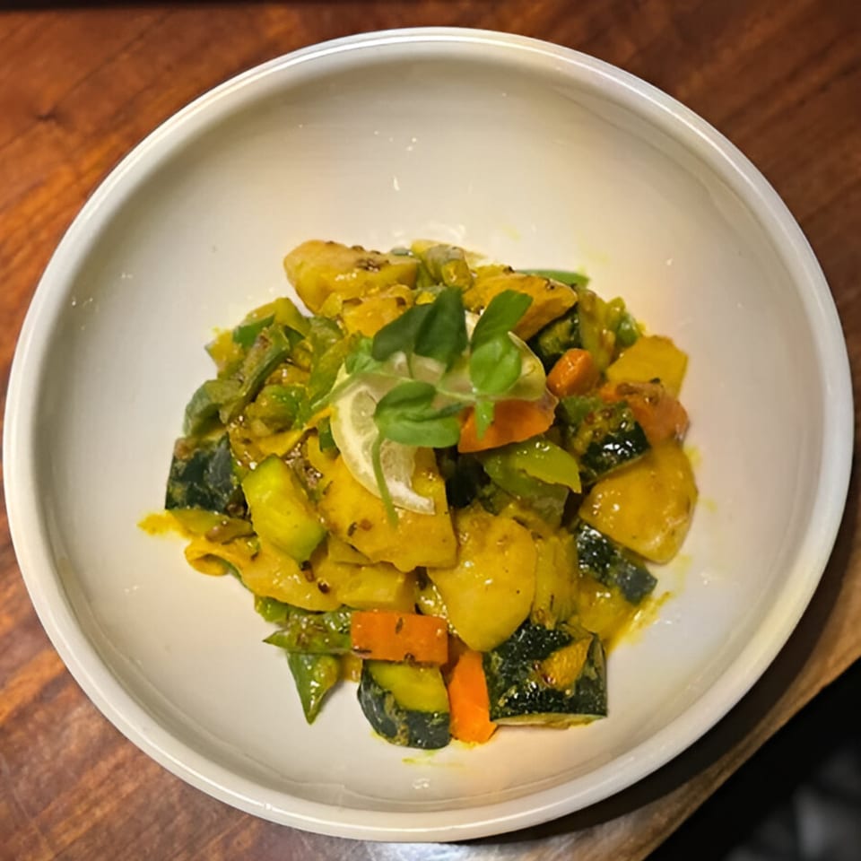 Nepalese vegetable curry with potatoes, zucchini, carrots, and green peppers, garnished with lemon and herbs.
