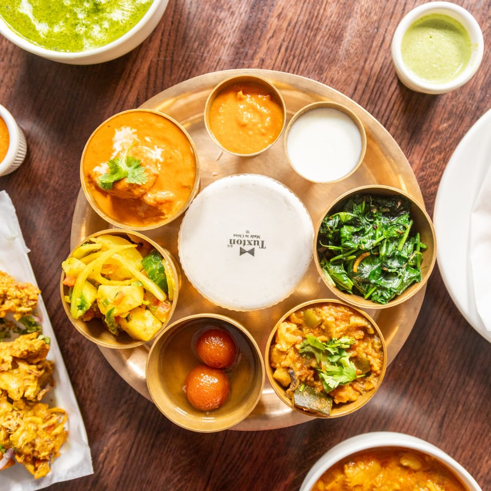 A Himalayan Cuisine thali with various small bowls of curries, vegetables, rice, and gulab jamun.