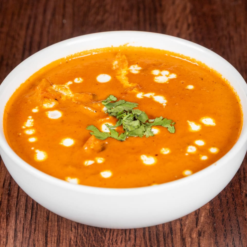 A white bowl filled with orange Nepalese curry, garnished with fresh cilantro and cream swirls.