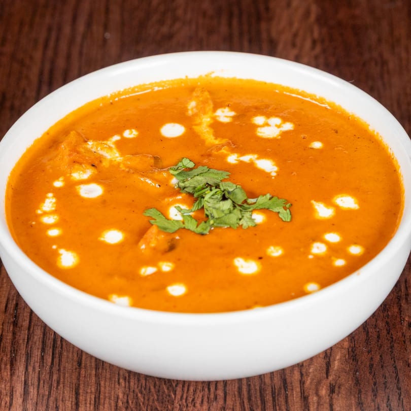 A white bowl filled with orange Nepalese curry, garnished with fresh cilantro and cream swirls.