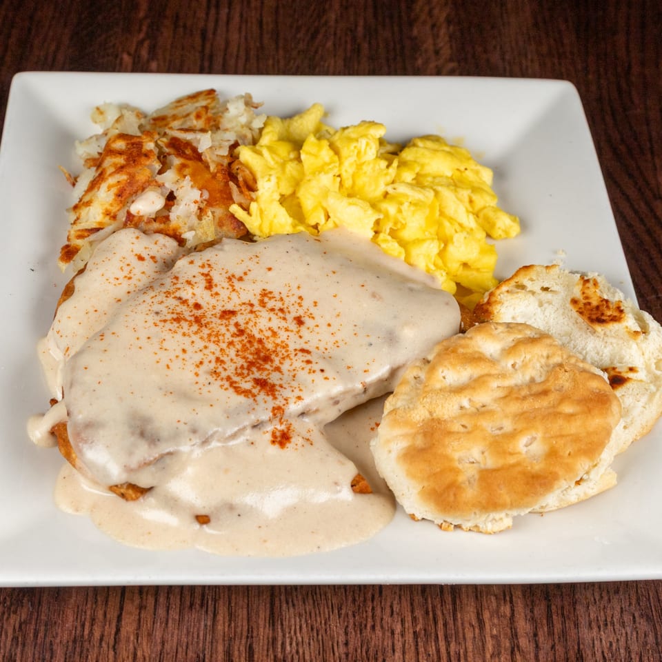 A breakfast plate with biscuits and gravy, scrambled eggs, and hash browns on a white plate.