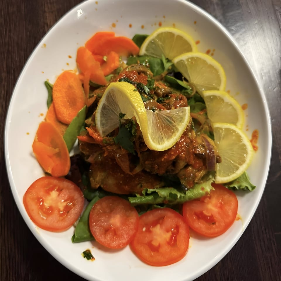 Nepalese chicken choila with lemon slices, tomatoes, carrots, and greens in a white bowl.